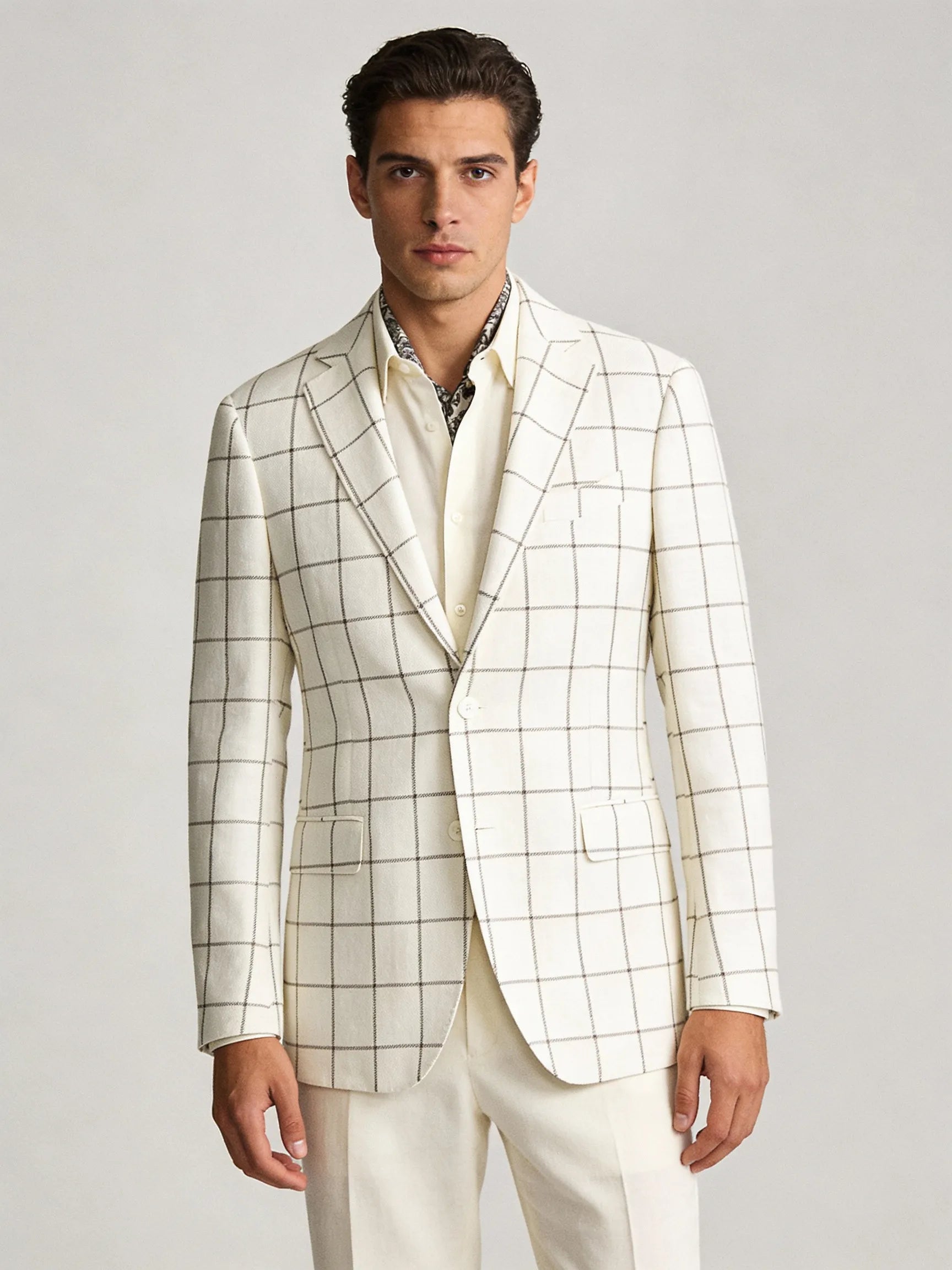 Man wearing a white checkered blazer over a patterned shirt on a light gray background