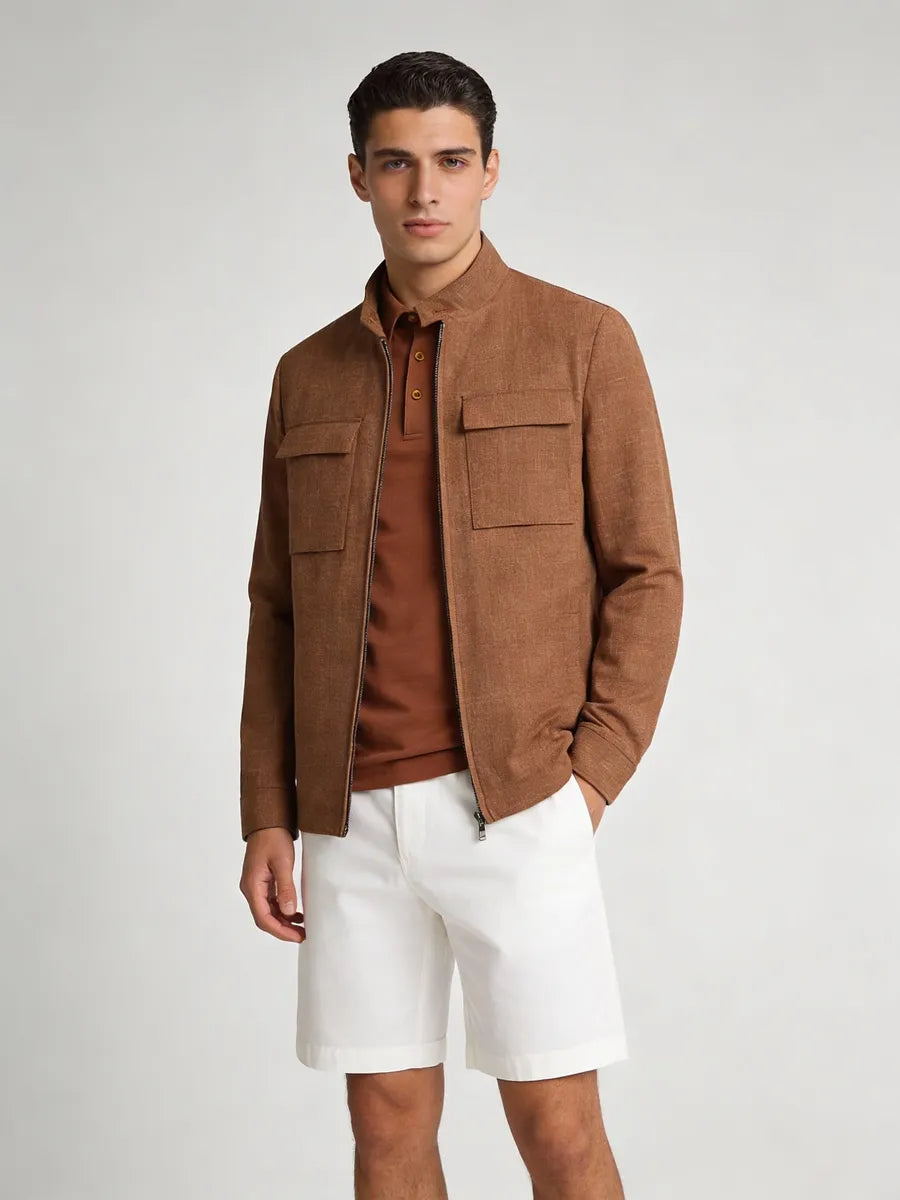 Man wearing a brown jacket over a brown shirt and white shorts on a light gray background