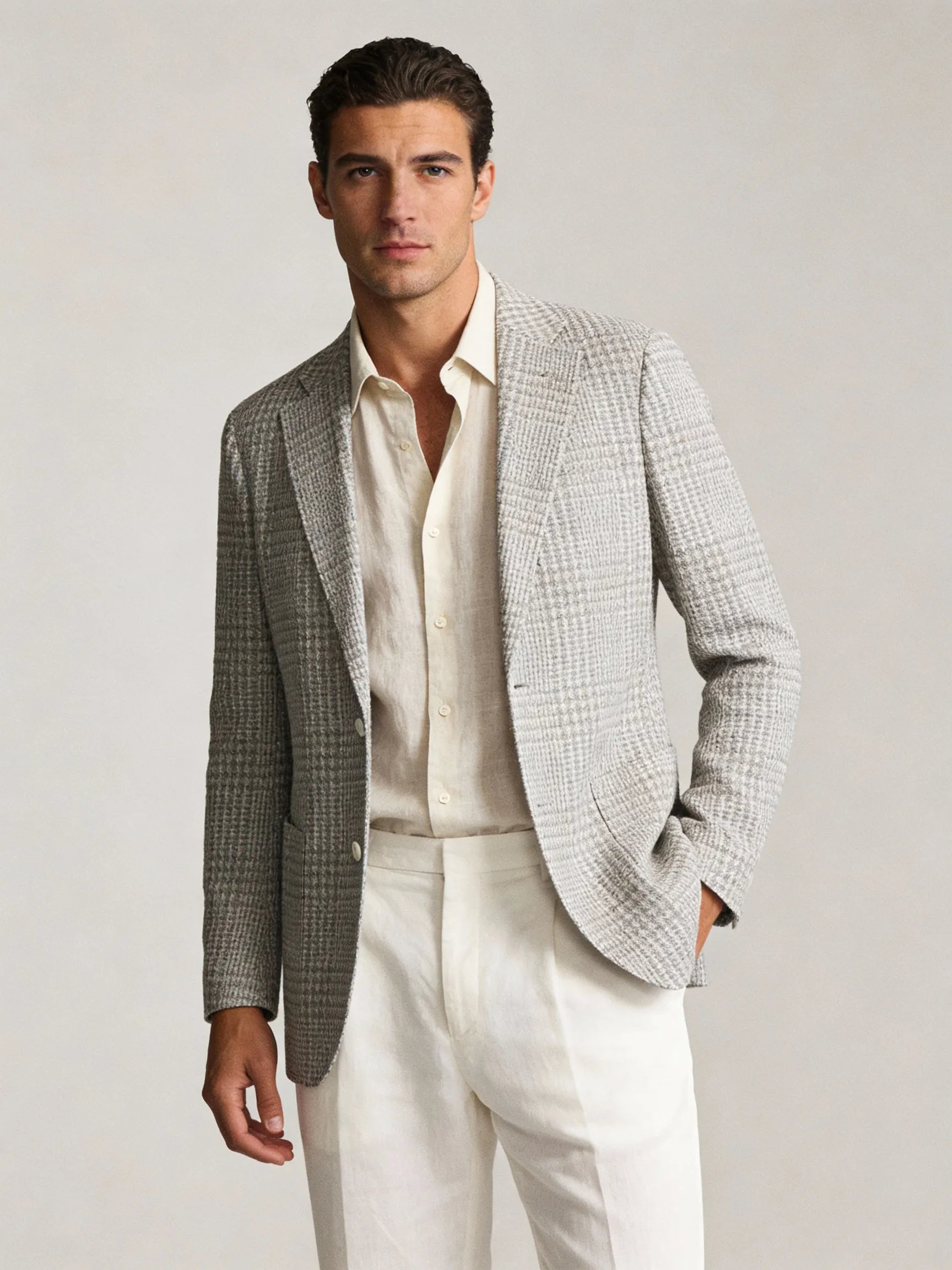 Man wearing a gray checkered blazer over a white shirt and pants on a plain background