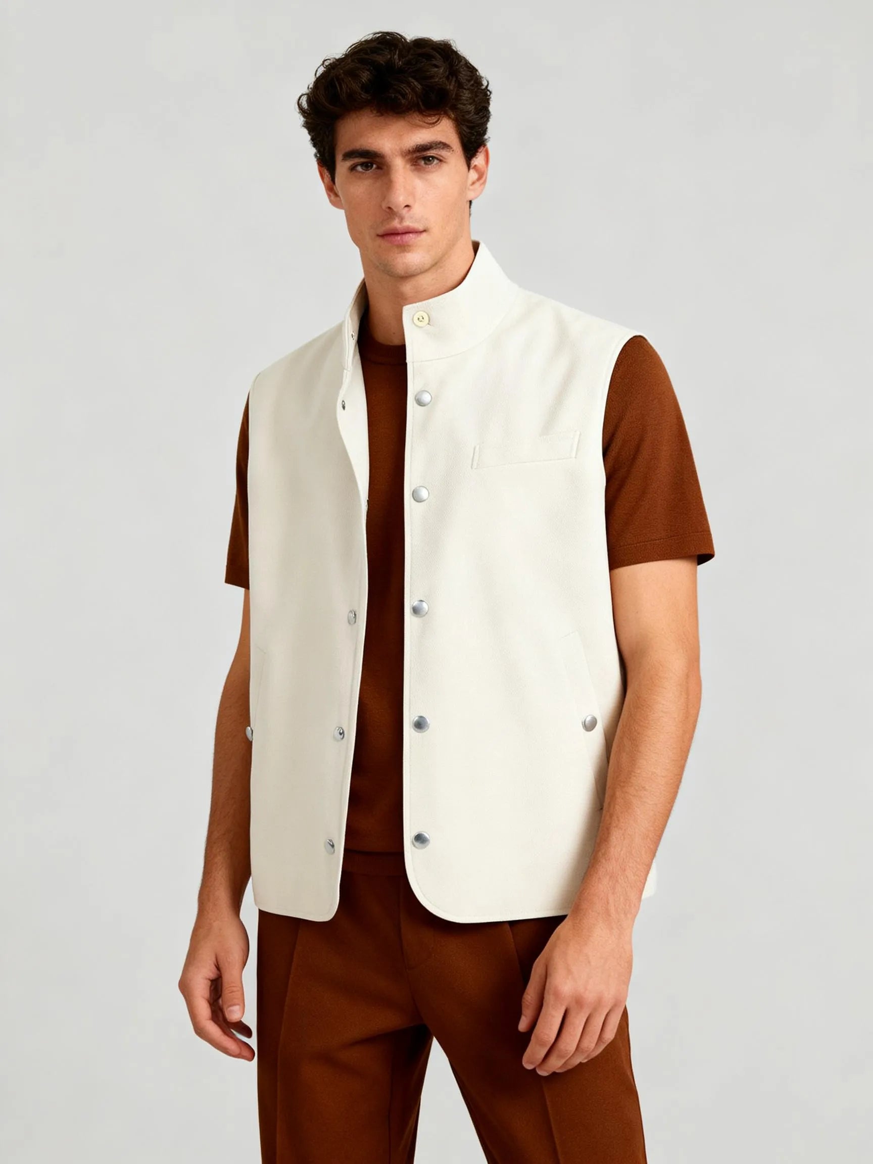 Man wearing a white vest over a brown shirt and pants on a light gray background