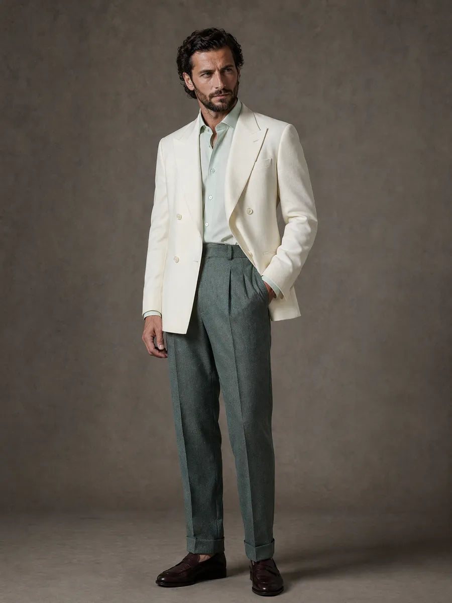Man wearing a white blazer, light blue shirt, and green pleated pants against a gray background