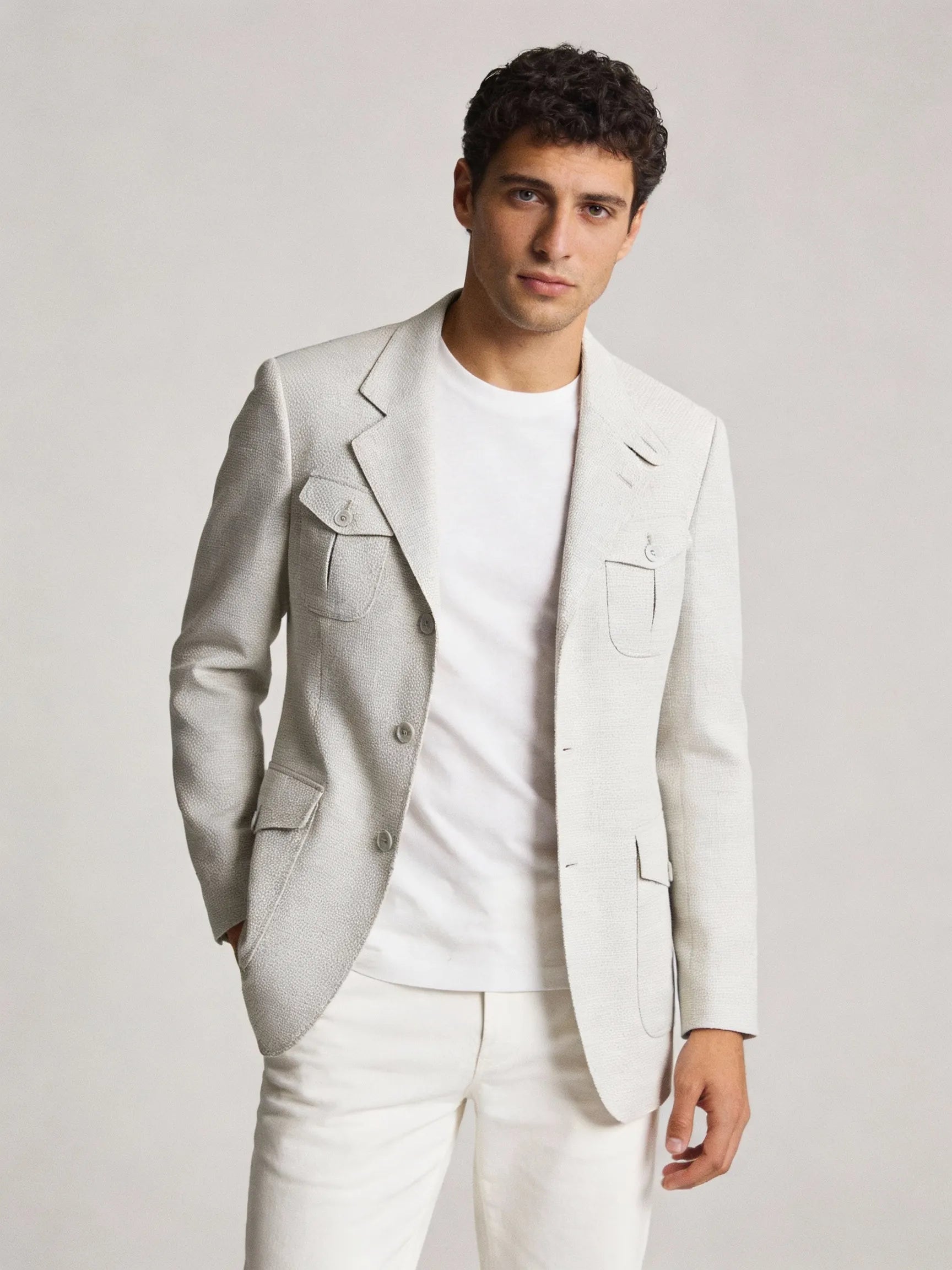 Man wearing a light gray blazer over a white shirt and pants on a plain background